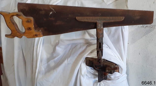 Metal vice is clamped in place and holds a hand saw in its jaws