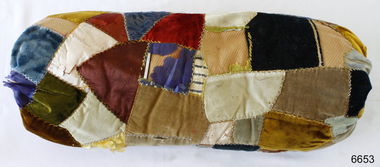 Sausage shaped patchwork cushion of various shapes and colours