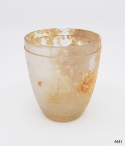 Glass, clear, wide mouth, sides slope inward towards base. Incrustations on surface