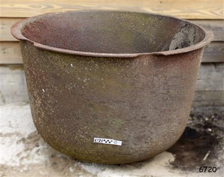 Round metal pot with rounded base and flat extended lip. Metal is rough, corroded and chipped.