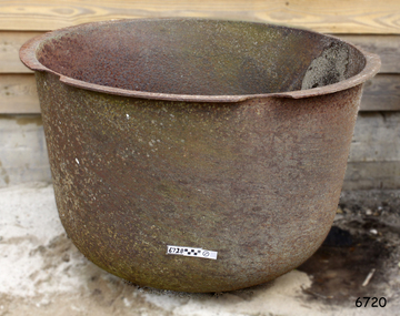 Round metal pot with rounded base and flat extended lip. Metal is rough, corroded and chipped.