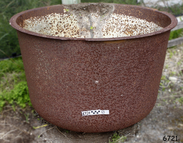 Round metal pot with rounded base and flat extended lip. Metal is rough, corroded and chipped.
