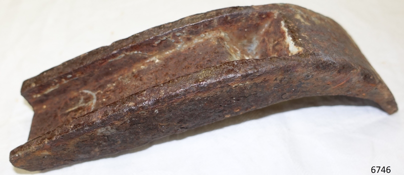 Iron piece is pitted and rusting. It is a curved shape with a formed channel along a portion of the centre