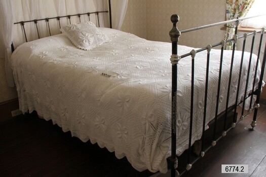 Cushion and bedspread, handmade, are laid out on bed. 