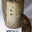 Grey clay pot with narrow base and pouring lip, encrustation on surface. Lid portion has small knob.
