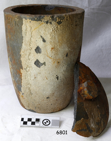 Grey clay pot with narrow base and pouring lip, encrustation on surface. Lid portion has small knob.