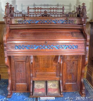 Wood encased organ with decorative fretwork and red and cream carpet-covered foot pedals