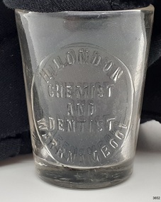 Clear medicine glass has embossed inscription of owner and address