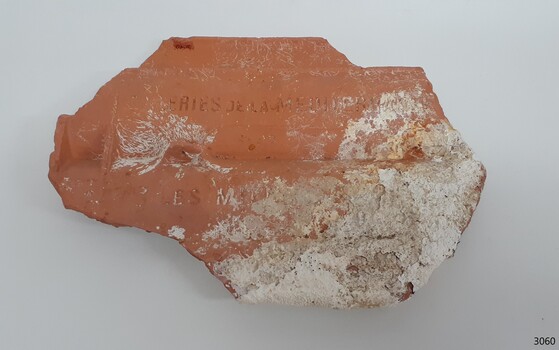 Orange tile shaped for roof covering, with encrustations on its surface