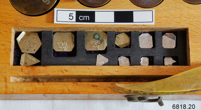 The 11 smallest metal weights nestled in the wooden box for use by an apothecary.