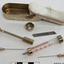 An oblong stainless steel metal box with lid, containing items comprising a syringe set, namely needles, plunger, cylinder, blade, etc.