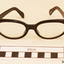 Black plastic rimmed reading spectacles in a tan case with printing in gold on the outside showing the maker's name and address.