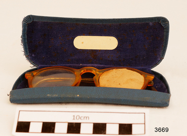 Orange rimmed glasses in blue case. One arm broken. Left lens blocked off with card. 
