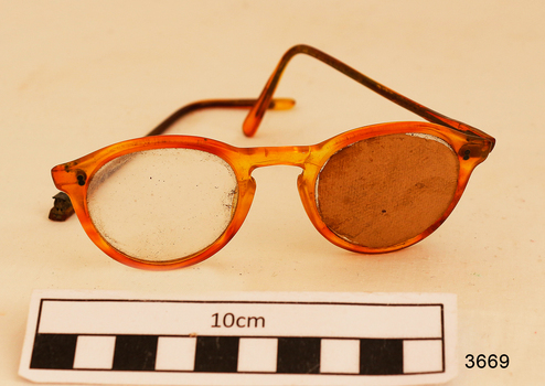 Orange rimmed glasses in blue case. One arm broken. Left lens blocked off with card. 