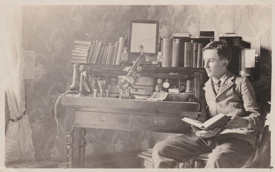 Sepia  photograph of a young man seated at a desk on which is medical instruments and books 