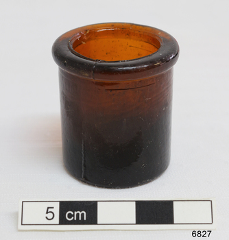 Small dark brown glass round pill or medication cup with heavy lip.