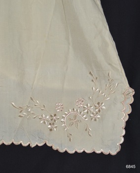 Floral design is embroidered onto the fabric. The edges are scalloped.