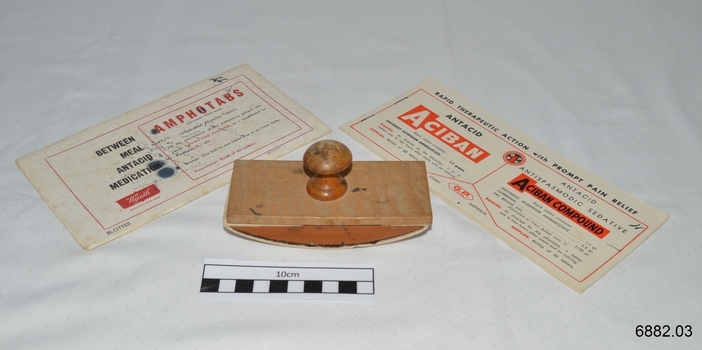 An oblong blotter with curved base and a handle on top. Two books of blotting paper also displayed, and sheets from them could be fitted onto the blotter for use.