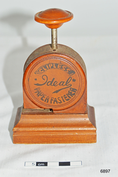 A bakelite and metal paper fastener. Round body with press handle at top.