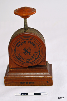 A bakelite and metal paper fastener. Round body with press handle at top.