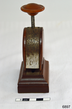 A bakelite and metal paper fastener. Round body with press handle at top.