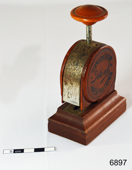 A bakelite and metal paper fastener. Round body with press handle at top.