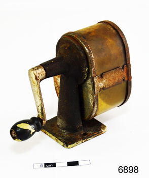 A metal desk pencil sharpener, with handle at rear, and aperture at front. Badly rusted.