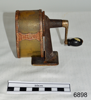  A metal desk pencil sharpener, with handle at rear, and aperture at front. Badly rusted.