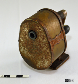 A metal desk pencil sharpener, with handle at rear, and aperture at front. Badly rusted.