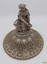 Close view of the silver lid with elaborate decoration and a semi-kneeling robed female figure