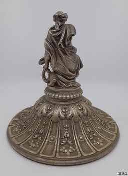 The figure on the lid is holding a wreath in each hand and appears to be bowling it
