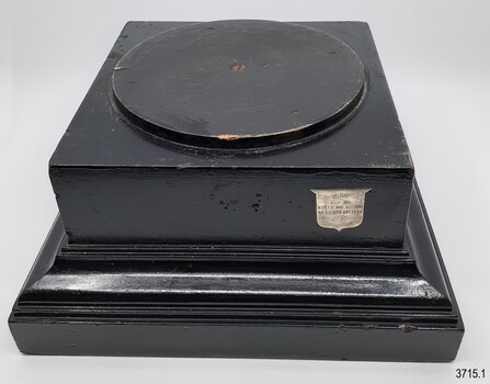 Black plinth has a round stand in the middle. A siield is on the right