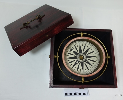Navigation compass withing the base of a wooden box, with lid beside it