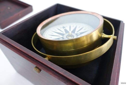Compass base within box, lid beside box. Compass is tilted on its gimbal.