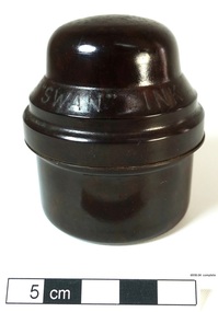 A small bottle of ink, sitting in a brown Bakelite screw top container, designed to protect it during travel.