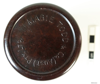 A small bottle of ink, sitting in a brown Bakelite screw top container, designed to protect it during travel.