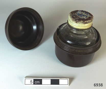 A small bottle of ink, sitting in a brown Bakelite screw top container, designed to protect it during travel.