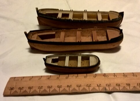 Set of three small model boats aligned with a ruler