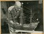 Sepia semigloss photograph with the maker Jim Williams applying touch up details to the model of “Sovereign of the Seas”. 