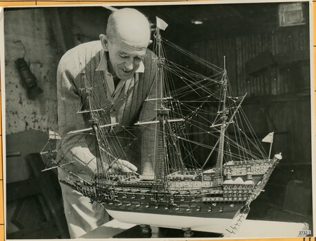 Sepia semigloss photograph with the maker Jim Williams applying touch up details to the model of “Sovereign of the Seas”. 