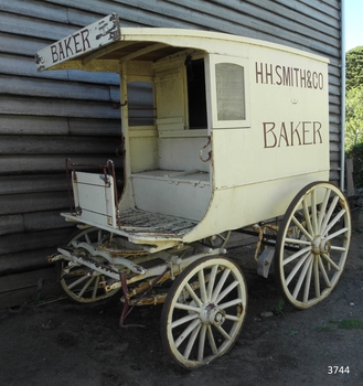 An 4 wheeled bakery delivery cart/wagon, painted in yellow with brown writing of the business name: H.R. Smith & Co, a Warrnambool baker.