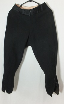 Dark fabric pants with silk waistband, tapered legs with buttons on the outer leg