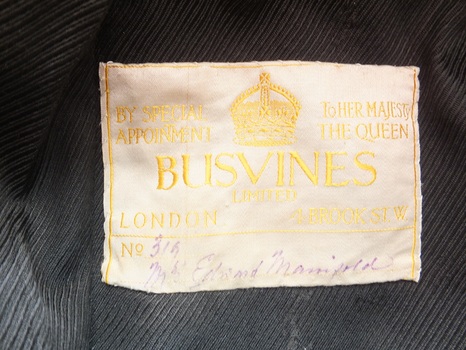 Cream fabric label with gold embroidered details and handwritten pen details