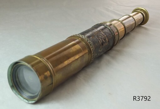 Telescope is shiny brass, in several telescoping sections, with leather hand grip 