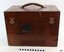 varnished wooden case, leather handle,  brass closures and metal hook closures. There is a circular attachment on the front.