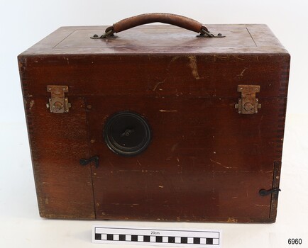 varnished wooden case, leather handle,  brass closures and metal hook closures. There is a circular attachment on the front.