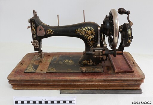 Machine has a black body with gold decals. It is hand crank operated.