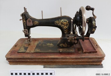 Machine has a black body with gold decals. It is hand crank operated.