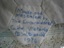 Embroidered inscription in blue thread on a plain hexagonal piece of fabric