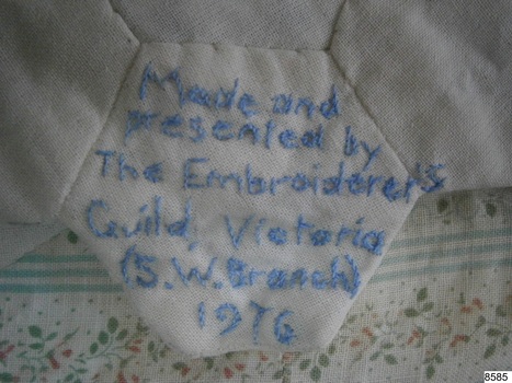 Embroidered inscription in blue thread on a plain octagonal piece of fabric
